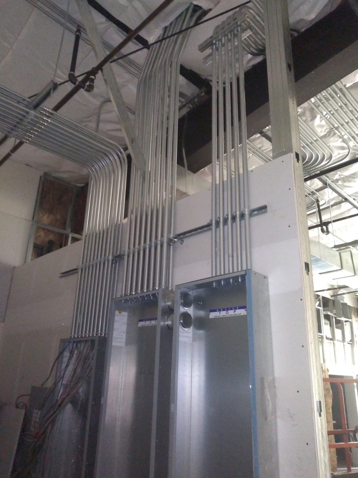 Parallel conduit risers bending into wall-mounted panelboards